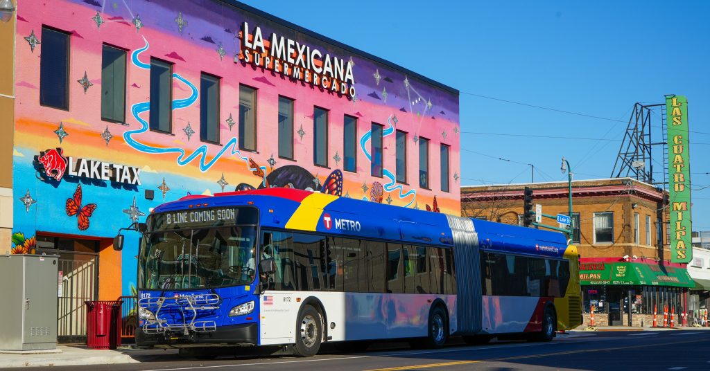 A new B Line bus -- extra long and painted blue, yellow and red -- in front of a colorful mural on Lake Street.