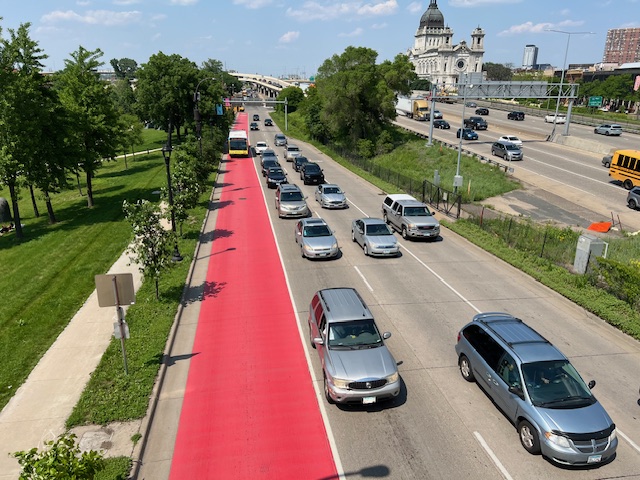 Traffic drives in three lanes parallel to a red-painted bus-only lane on Hennepin Avenue in Minneapolis