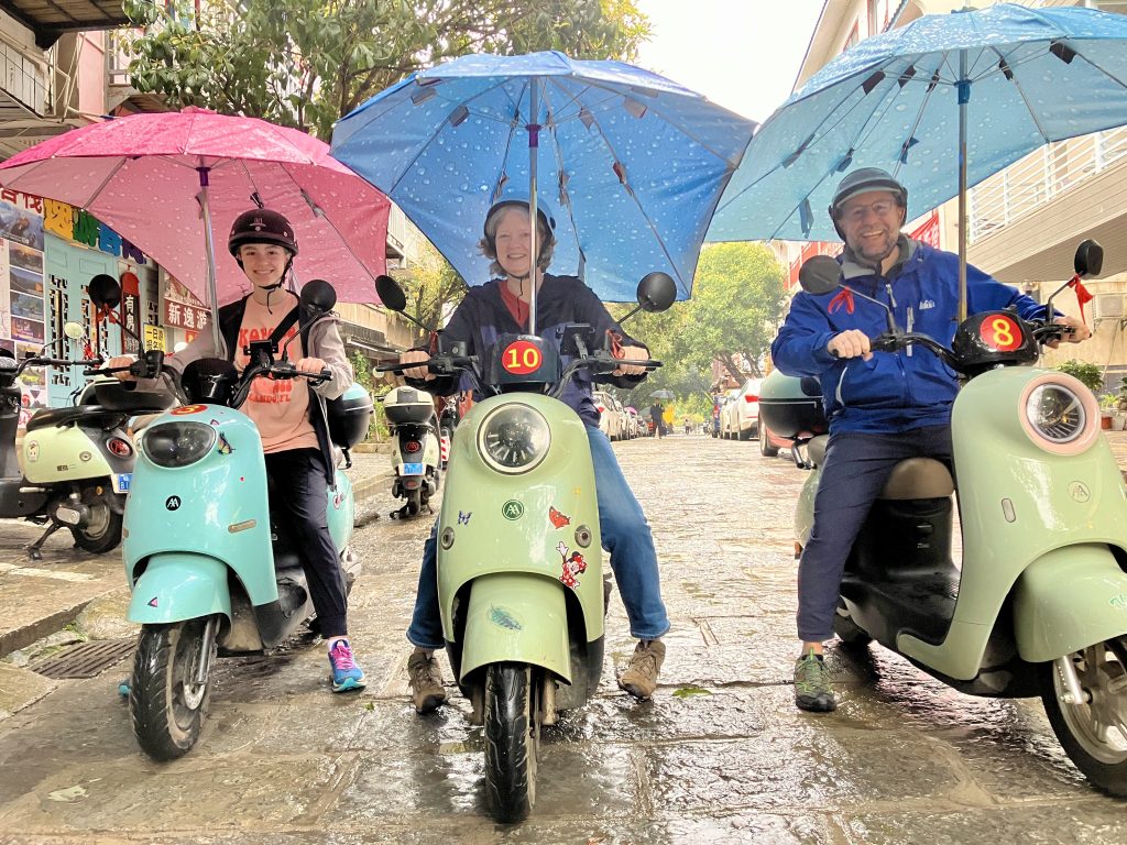 Author and his family, each on an electric, seated scooter, outfitted with rain umbrella