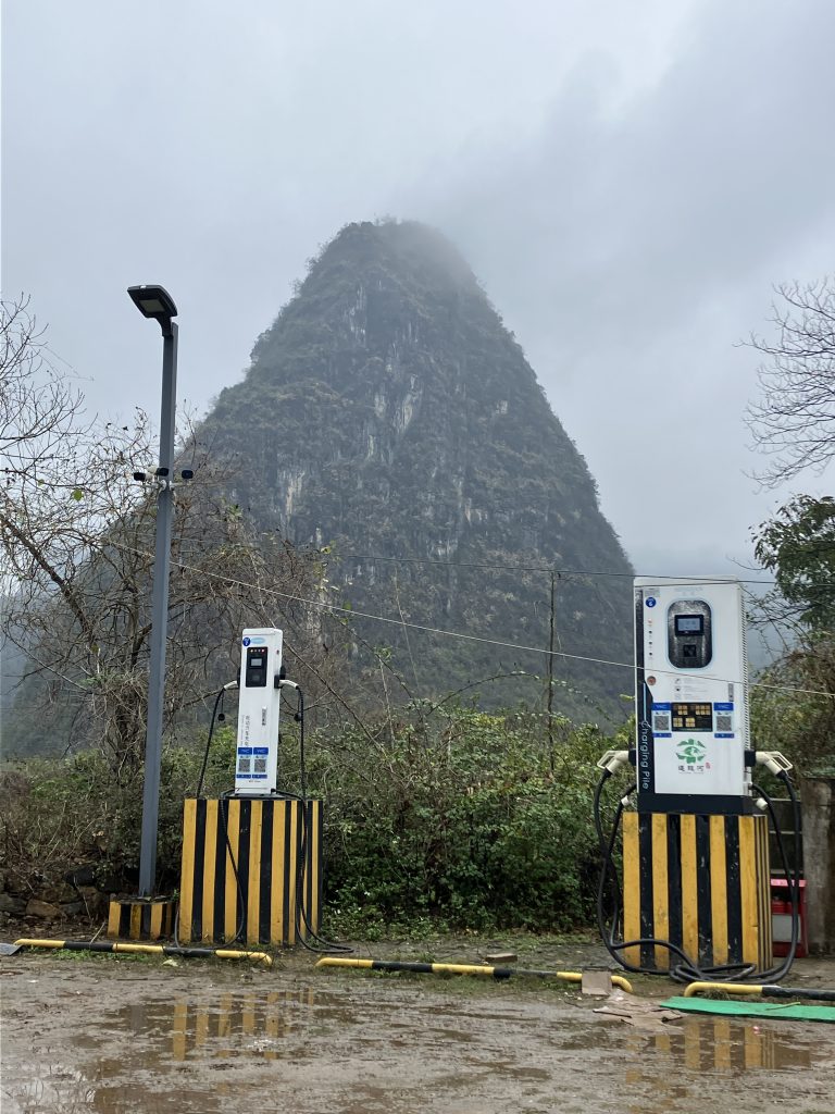 Electric vehicle charging stations in the foreground, massive karst peaks in the background