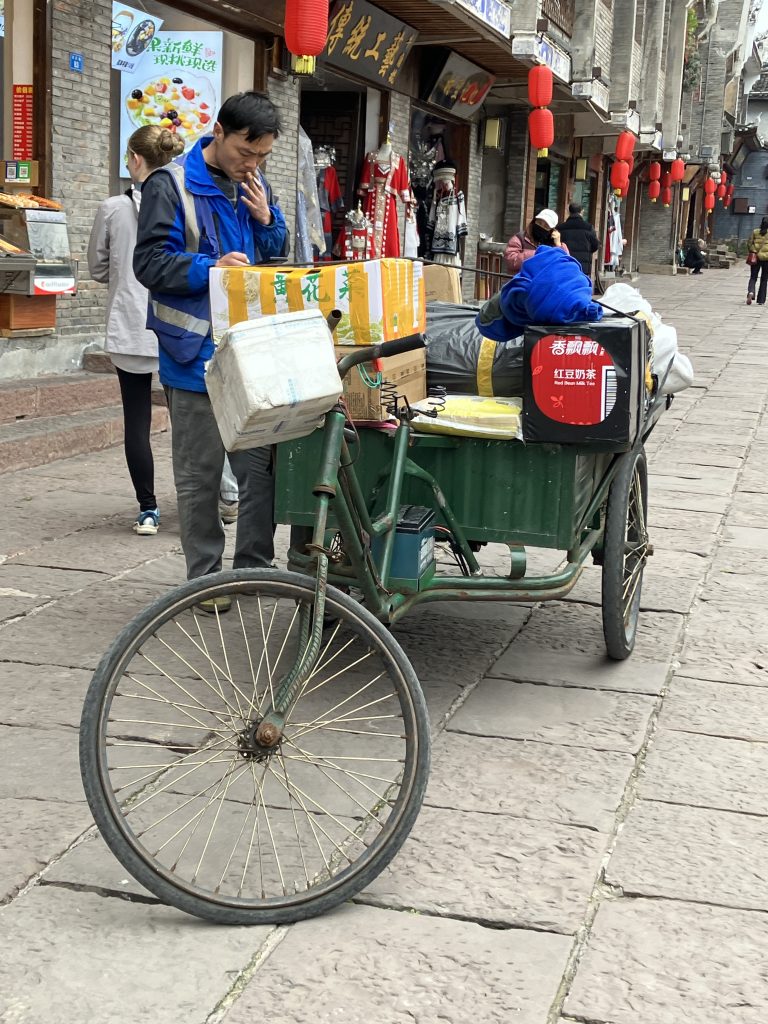 Delivery person checking his phone next to his adult tricycle loaded with packages.