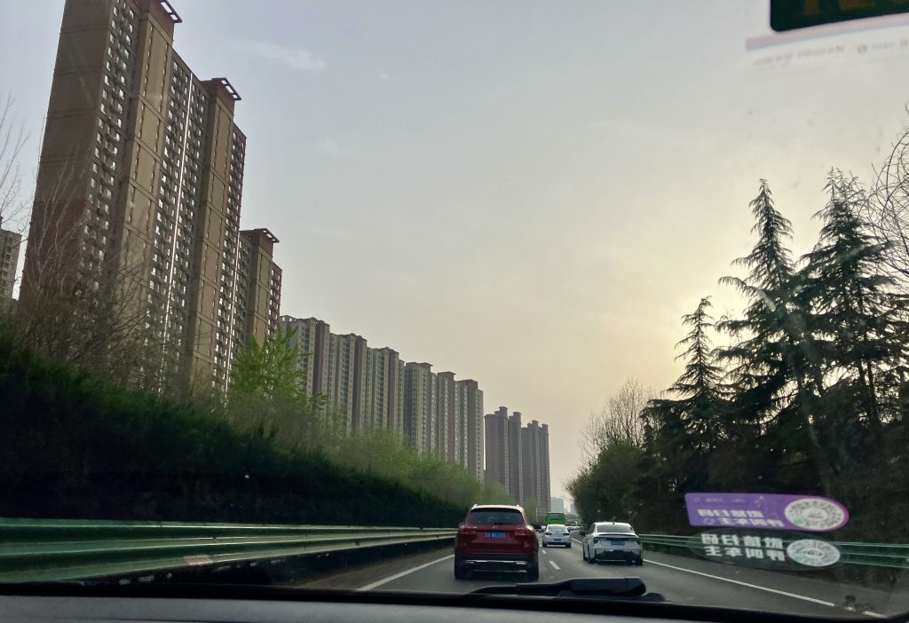 A narrow highway lined with high foliage, and massive skyscrapers in the background