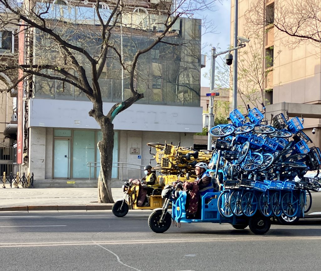Two motorized, three wheeled vehicles piled high with bike share bikes.