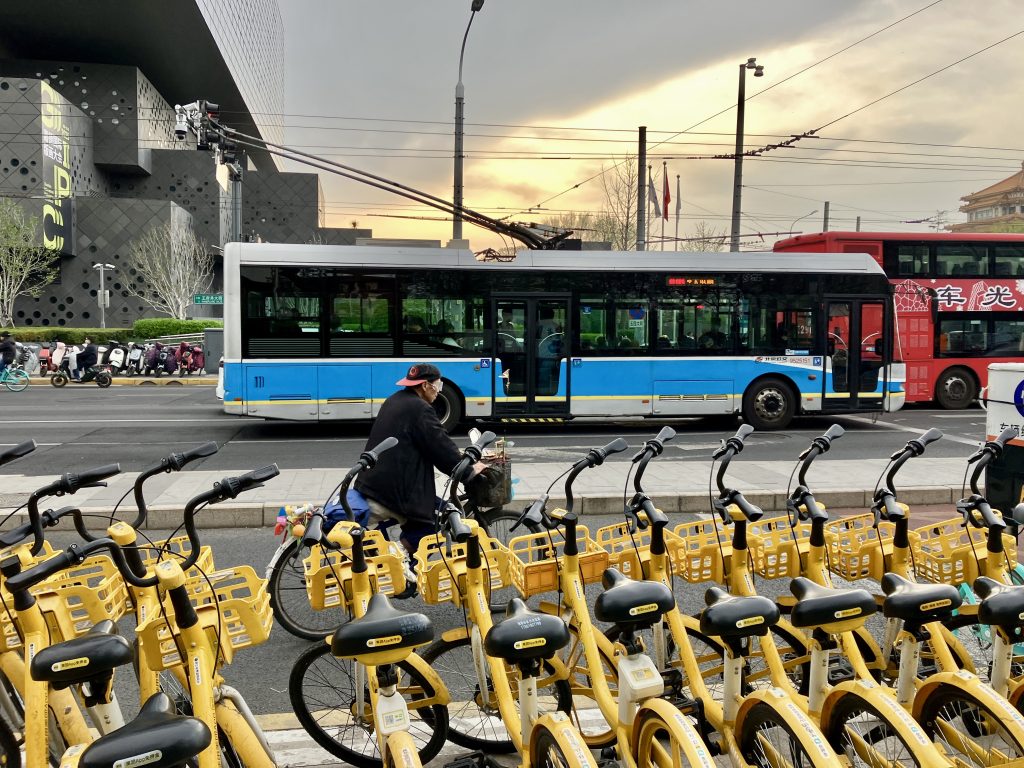 A row of yellow electric bikes,, with electric buses in the background