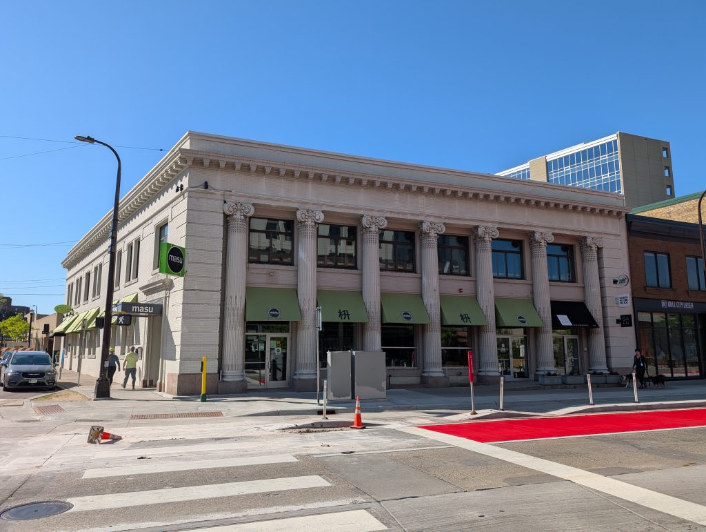 Street corner with light-colored building featuring seven columns in a variant of the Ionic or composite order