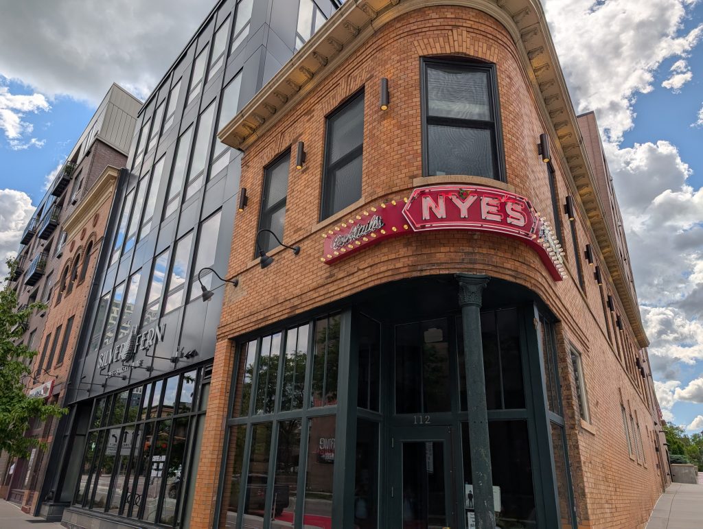 Curved corner entry of a two-story brick-faced  building with neon signage as Nye's.