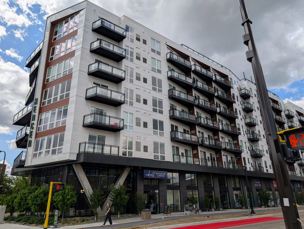 Light colored contemporary apartment building viewed from the narrow end of its wedge shape.