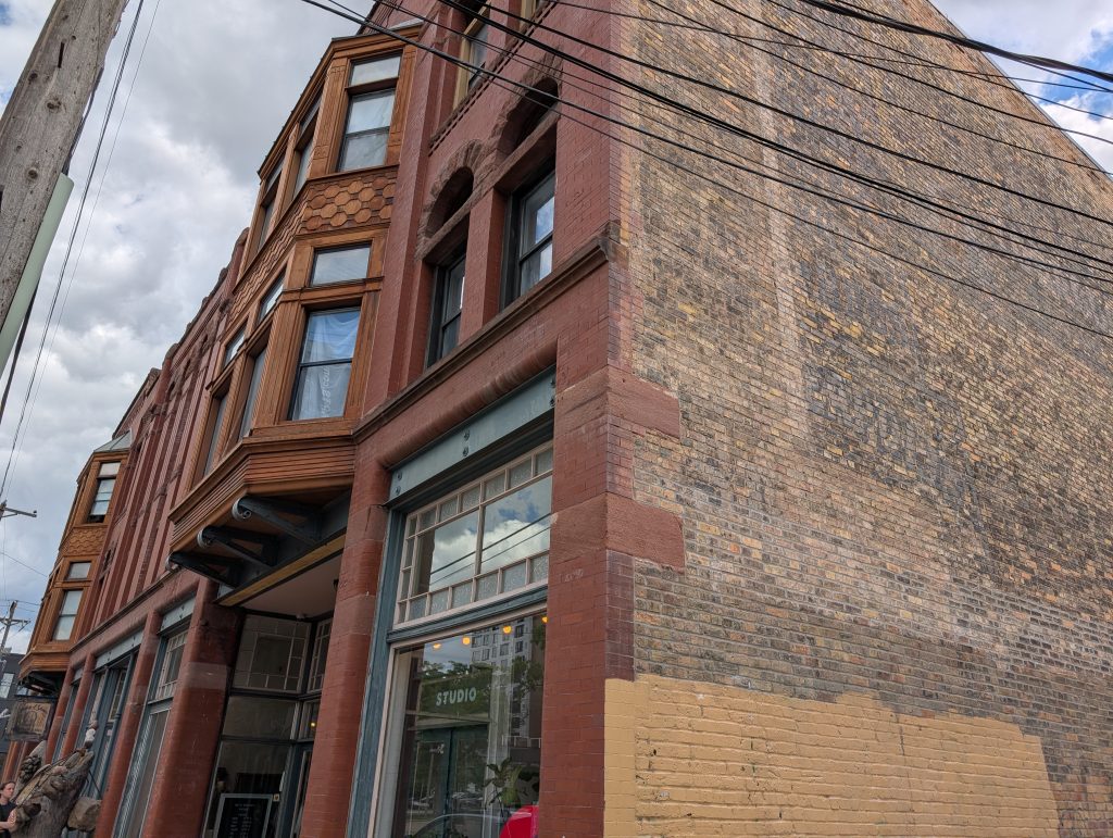 three-story brick building with bay windows, romanesque arches, pilasters, and quoins.