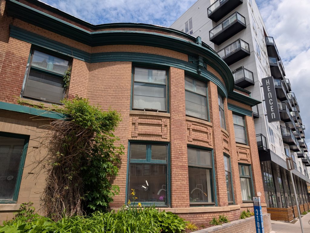 Bow-fronted two-story building; each level has three windows on the bowed portion and an additional window to each side; the left-hand window on the lower level is in a distinct protrusion and is different in style.