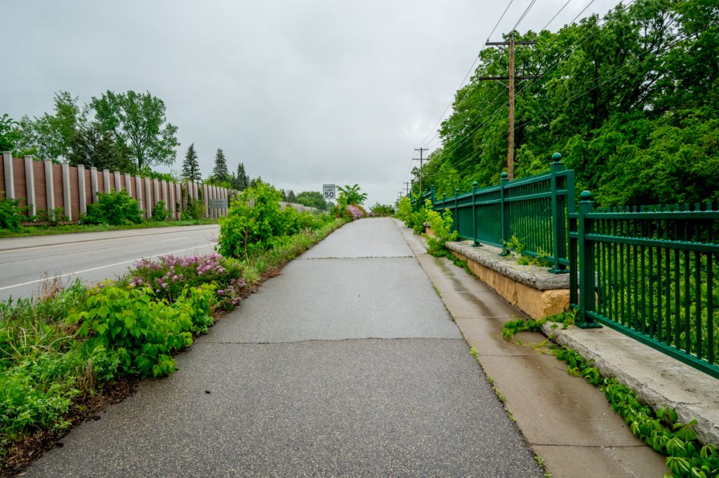 A paved path and street with greenery on the edges