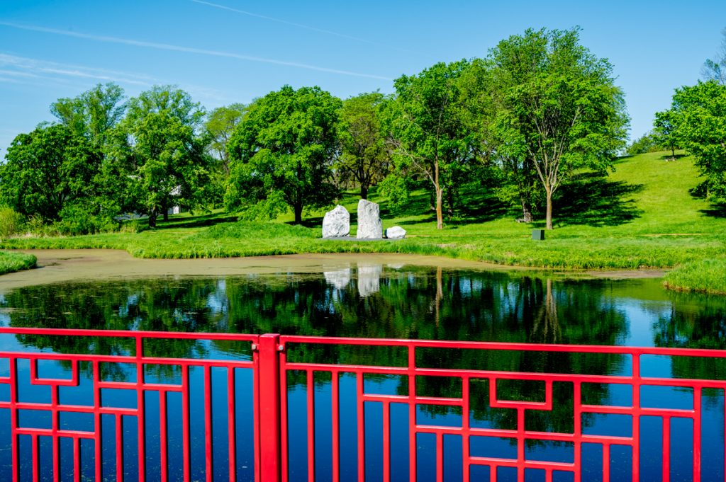 A red fence in front of a pond and greenery at the Minnesota Landscape Arboretum 
