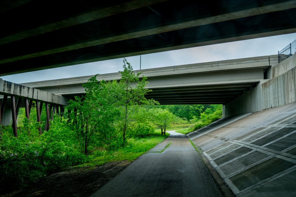 A trail on an underpass of two highways with greenery surrounding