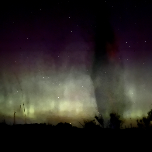 A long exposure of the author dancing in a dress while the northern lights dance in the background. The stars glow proudly like when someone squeezes your hand because they really like you.
