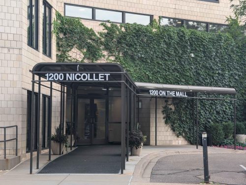 The outdoor entrance to the condo building 1200 Nicollet Mall, with white bricks and a black awning.