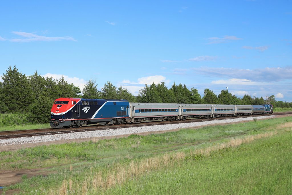 An Amtrak train in red, black, blue and silver color scheme running along a track in the countryside. 
