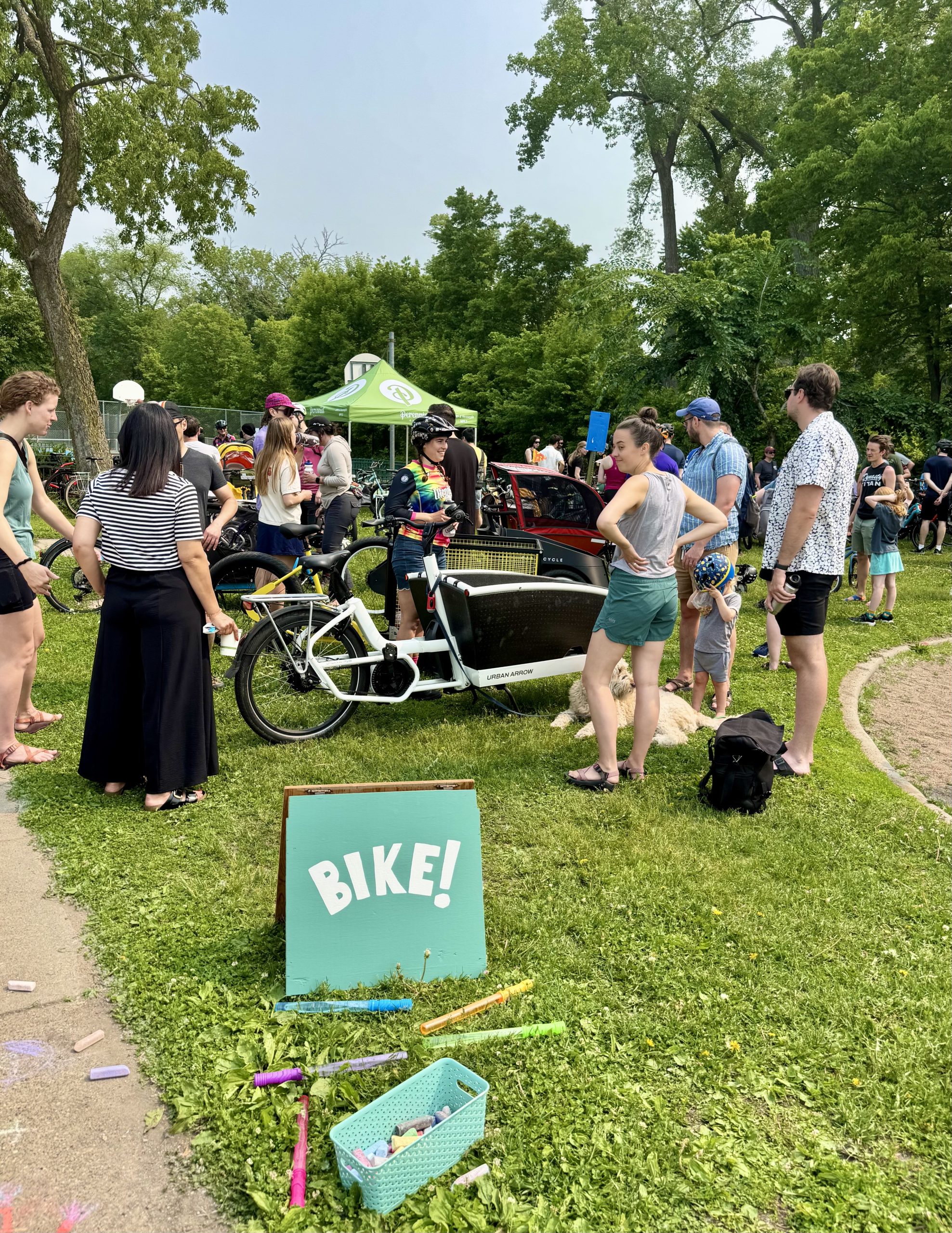 A green lawn sign says "Bike!" in front of a group of people gathered around a cargo bike.