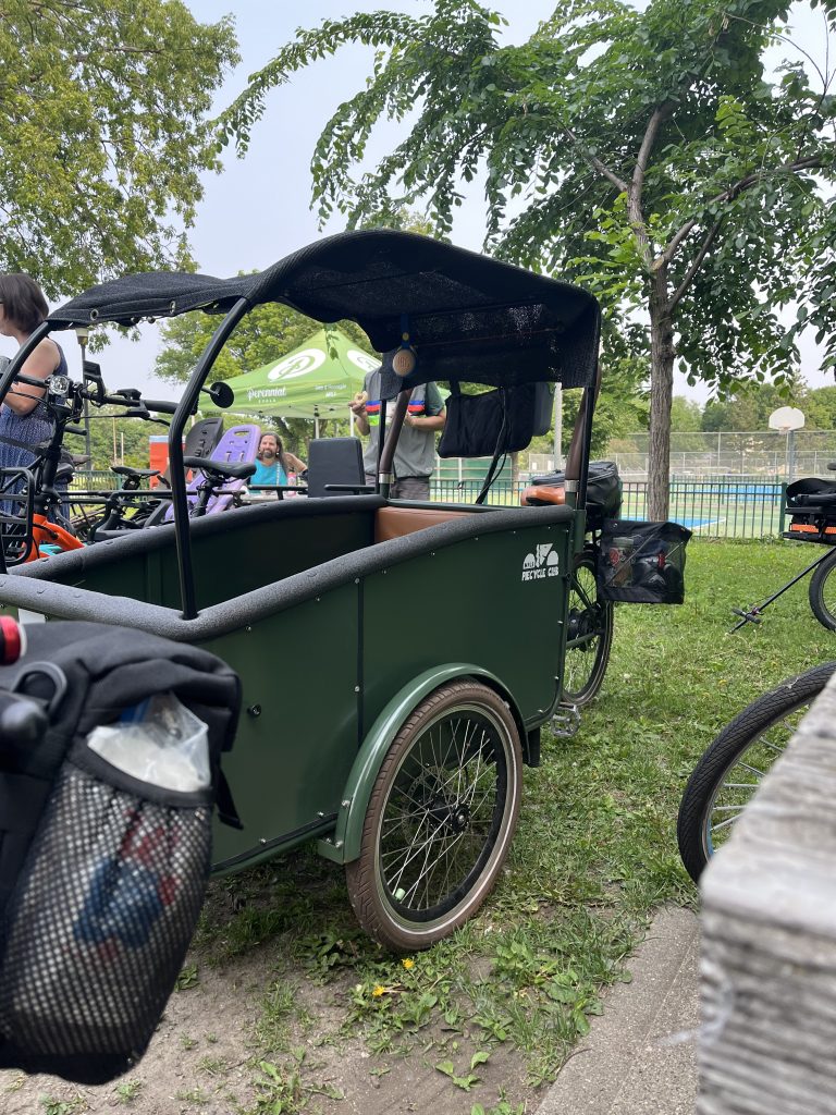 A green passenger compartment with a black canvas roof attached to a cargo bike out of frame.
