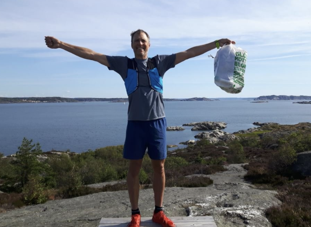 A person holding a bag of litter with a large body of water behind them.