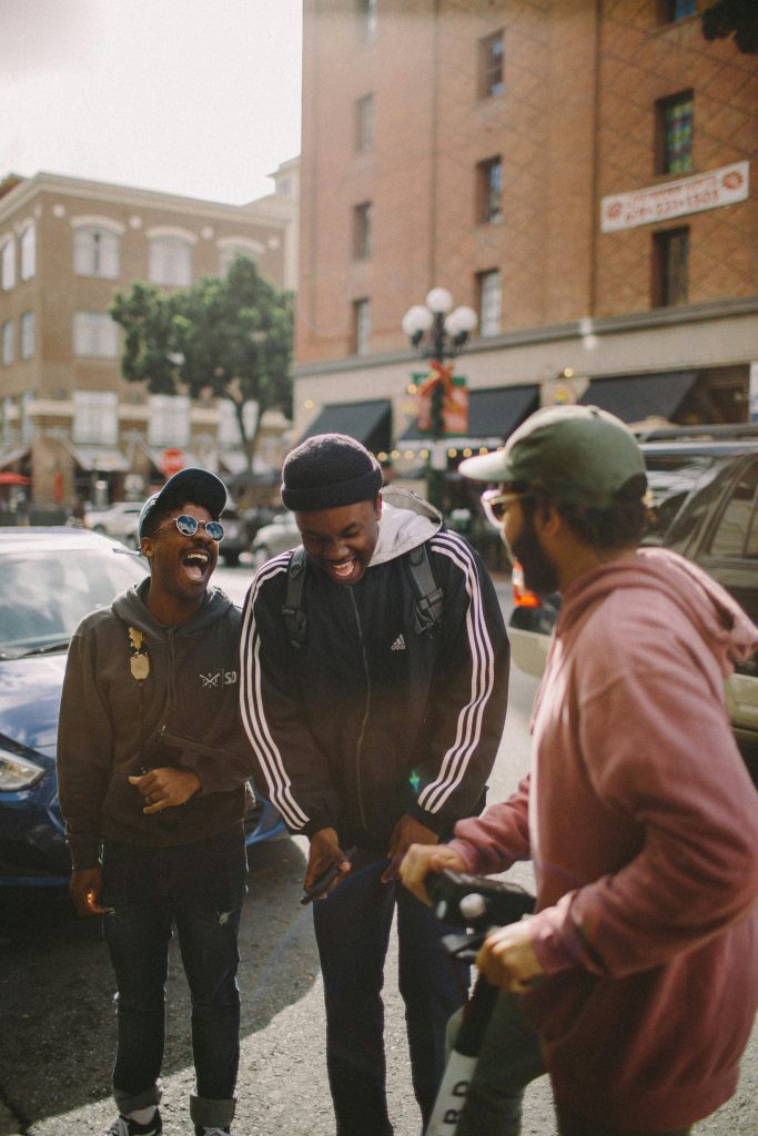 Three young men stand on the street laughing.