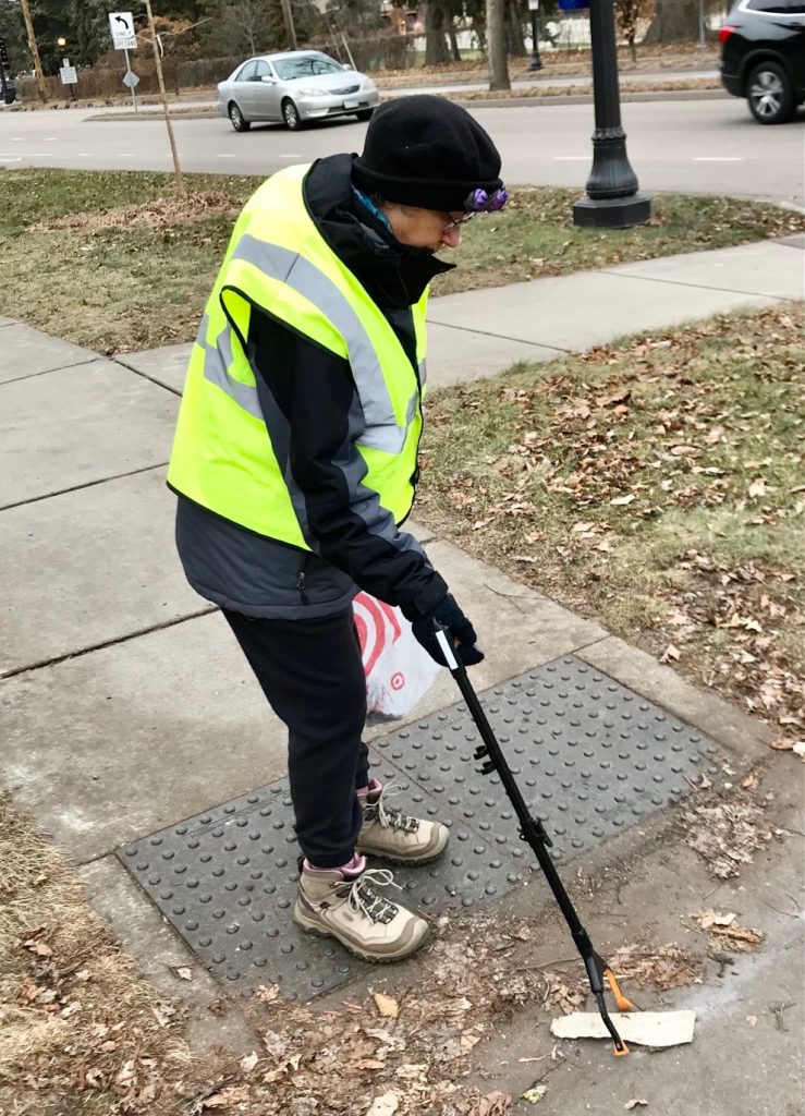 Person in a reflective vest using a grabber to pick up litter.