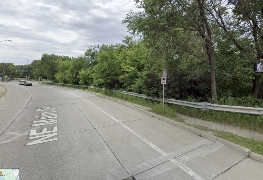Street view with cars, a guardrail, and trees in the background