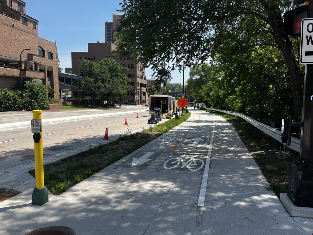 Shared bike and pedestrian sidewalk separated by grass and a curb. Car lane is to the left of the curb.