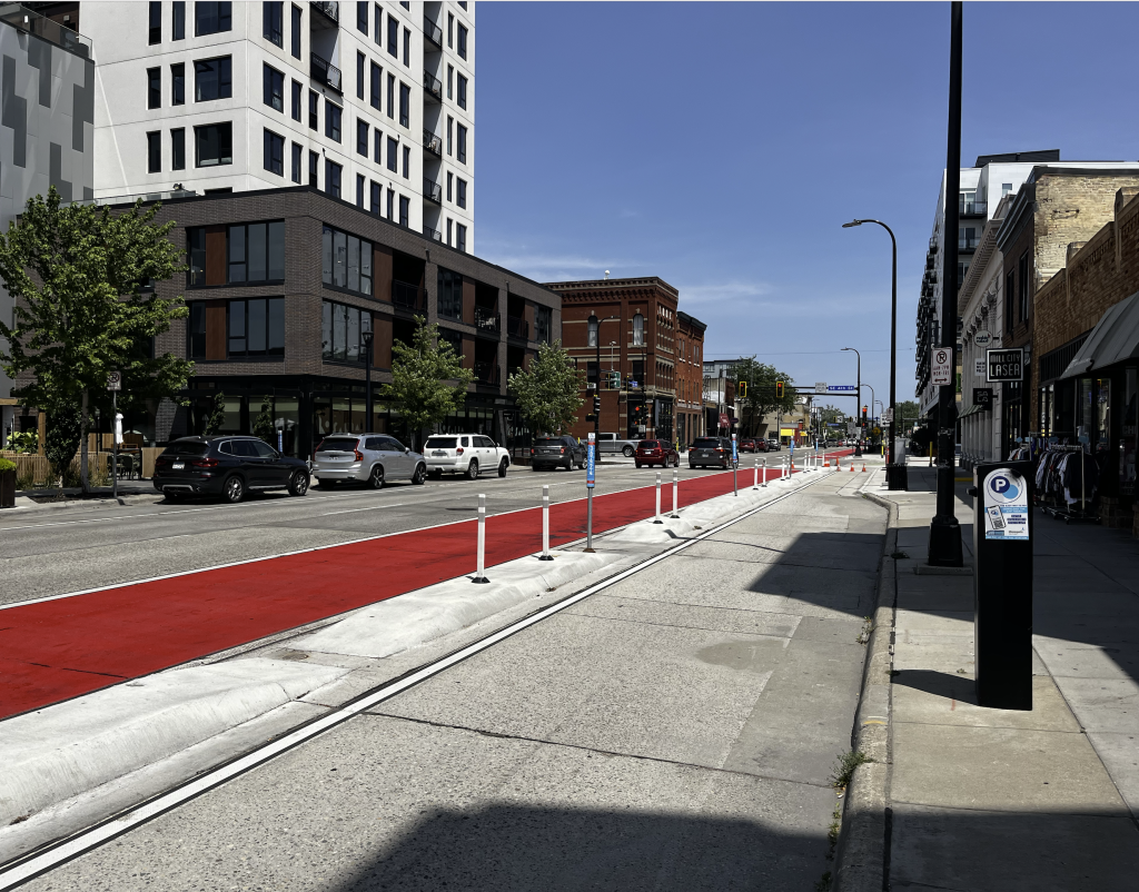 Street with car lanes, a red bus lane, and a bike lane with concrete divider separating it from the bus lane