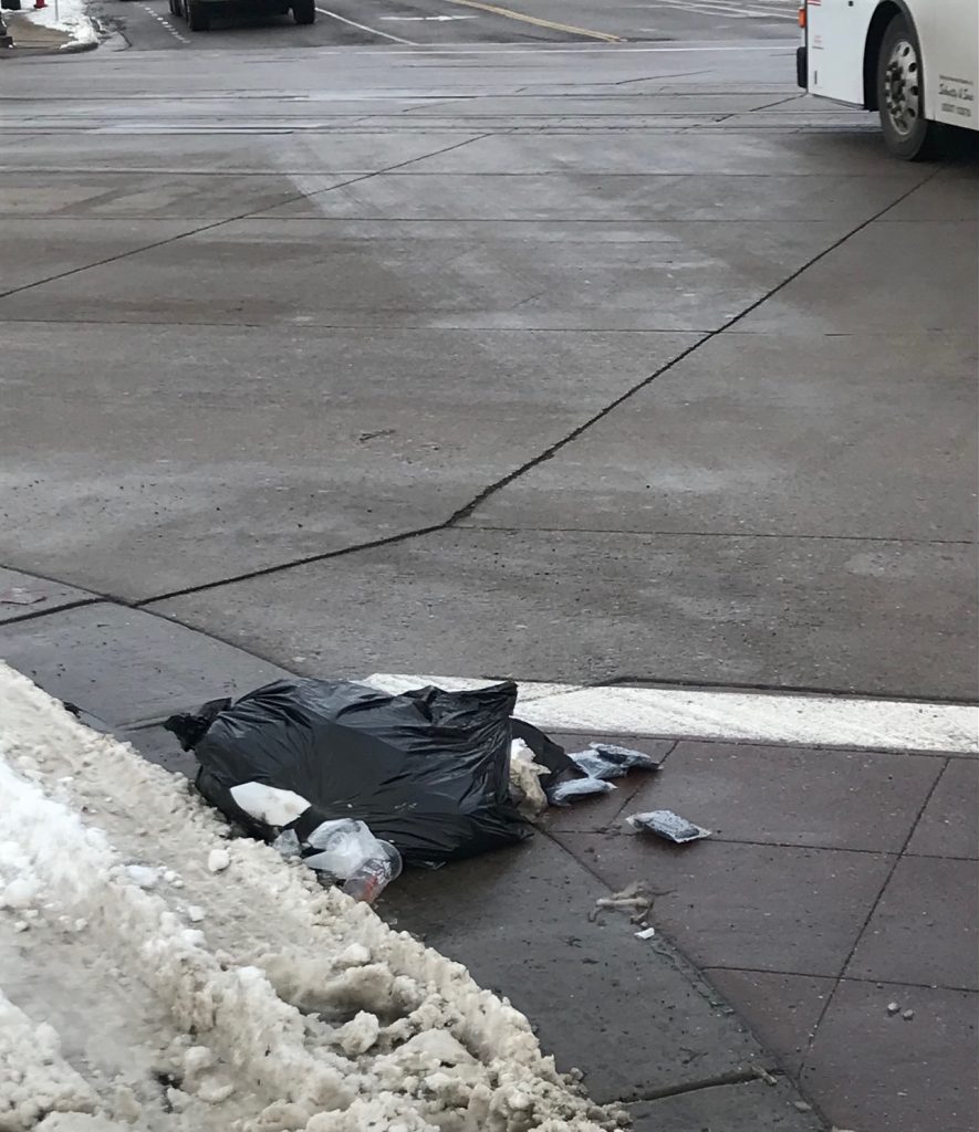Torn open garbage bag littered on the street.