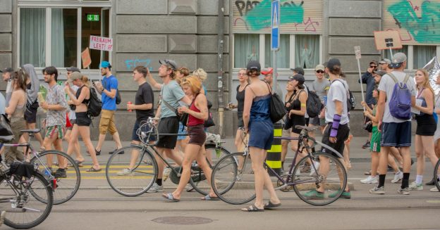 A group of people, on bikes and off, move down a city street.
