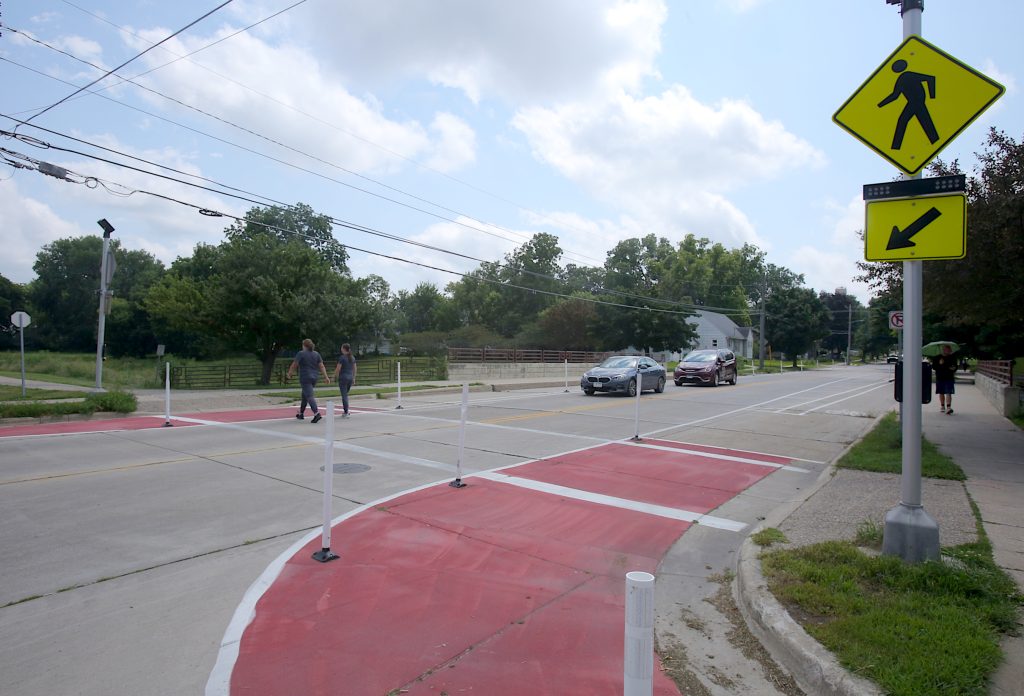 The new trail crossing creates more space for pedestrians with bollards extending in to the street and red paint to delineate bike lanes.