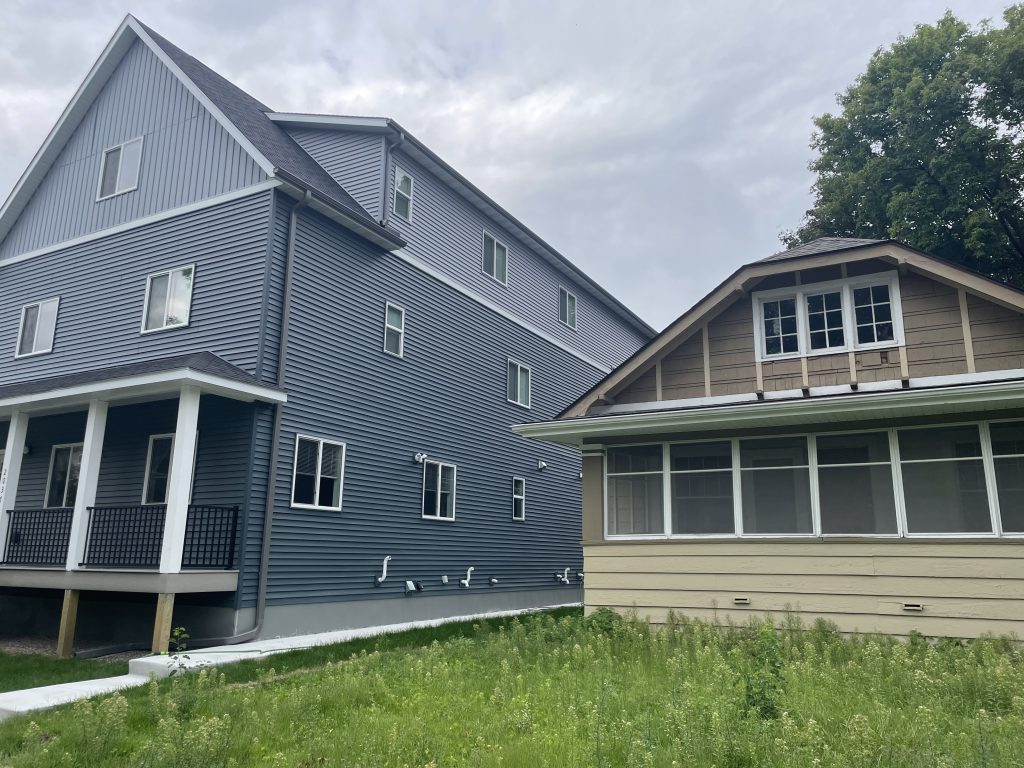 A multi-story, flat-faced blue apartment building, constructed for students, sits next to a small, abandoned single-family home near the St. Thomas campus.