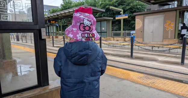 The back of a 6-year-old girl in a Hello Kitty pink hat waits at a Green Line station.