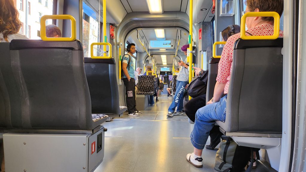 An aisle view of a tram in Berlin, with one man standing in a soccer jersey and the backs of others' heads as they ride.