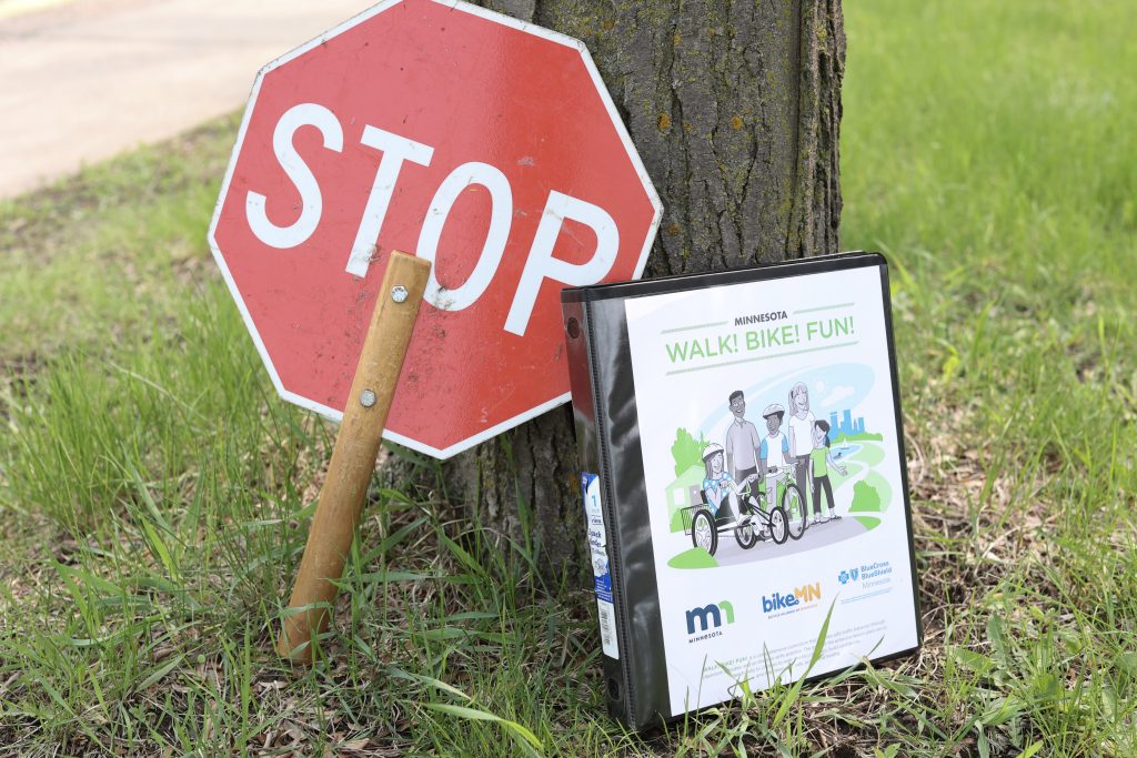 A red STOP sign on a stick and a Walk-Bike-Fun manual lean against a tree. Photo: BikeMN