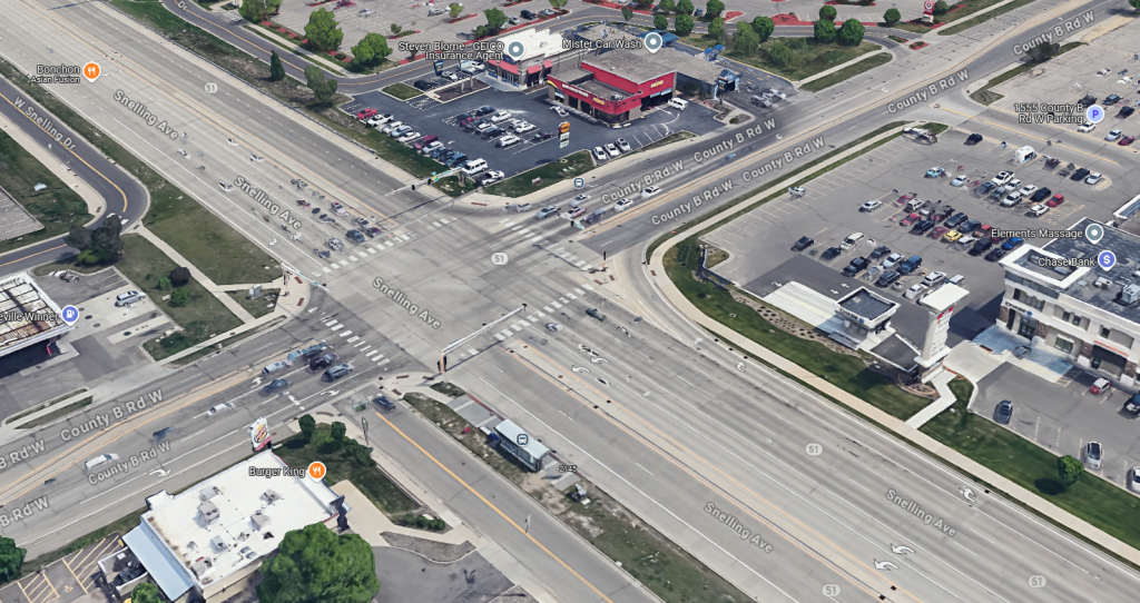 An aerial view of the wide intersection of Snelling Avenue and County Road B in Roseville, Minnesota, with multiple turn lanes and large parking lots nearby.