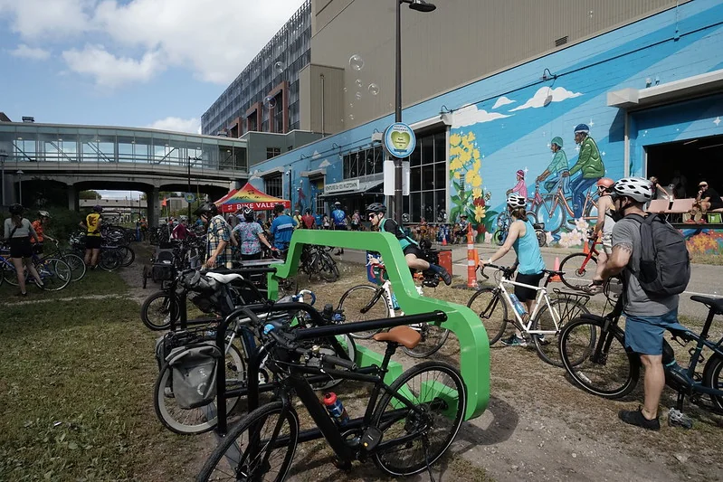 Crowd of people and bicycles outside a bike shop with colorful murals, on the Midtown Greenway.