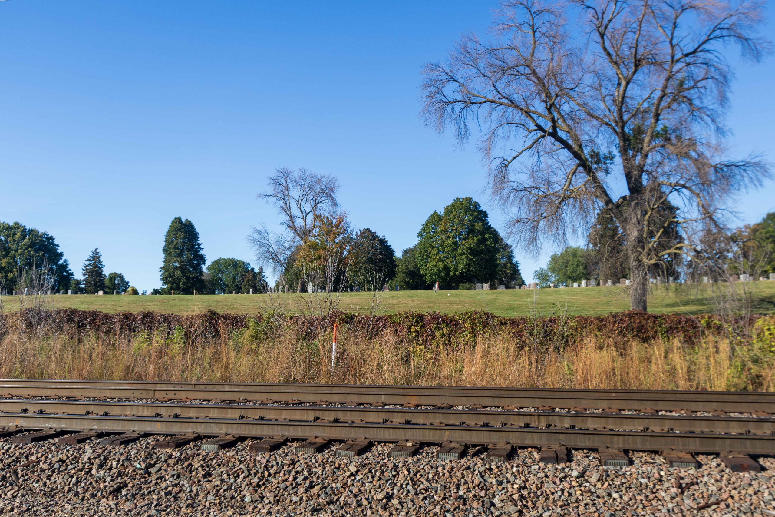 Gravel and railroad tracks in the foreground, brush and Calvary Cemetery in the background.