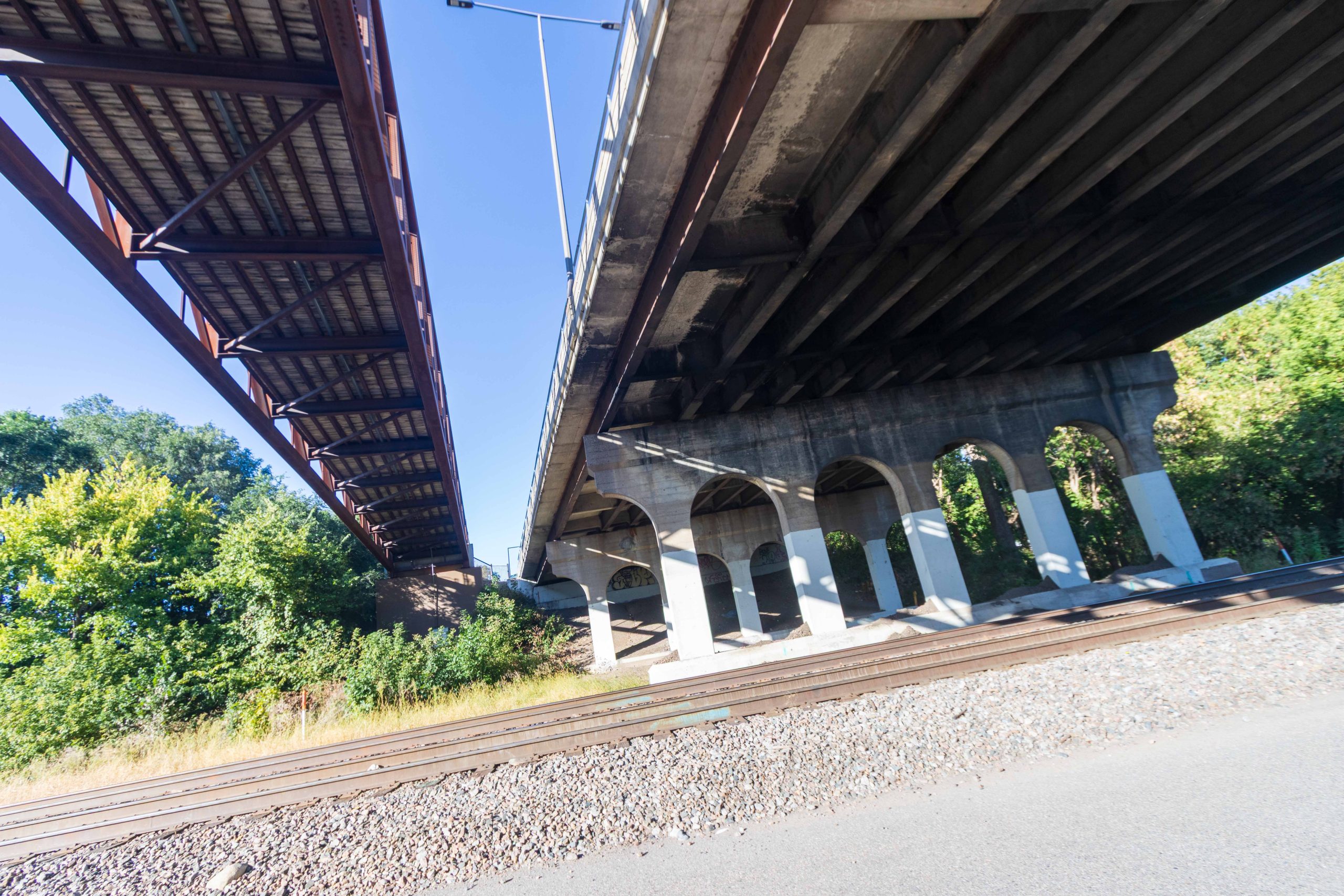 Railroad tracks in foreground and two bridges above, one pedestrian bridge and one for motor vehicles.