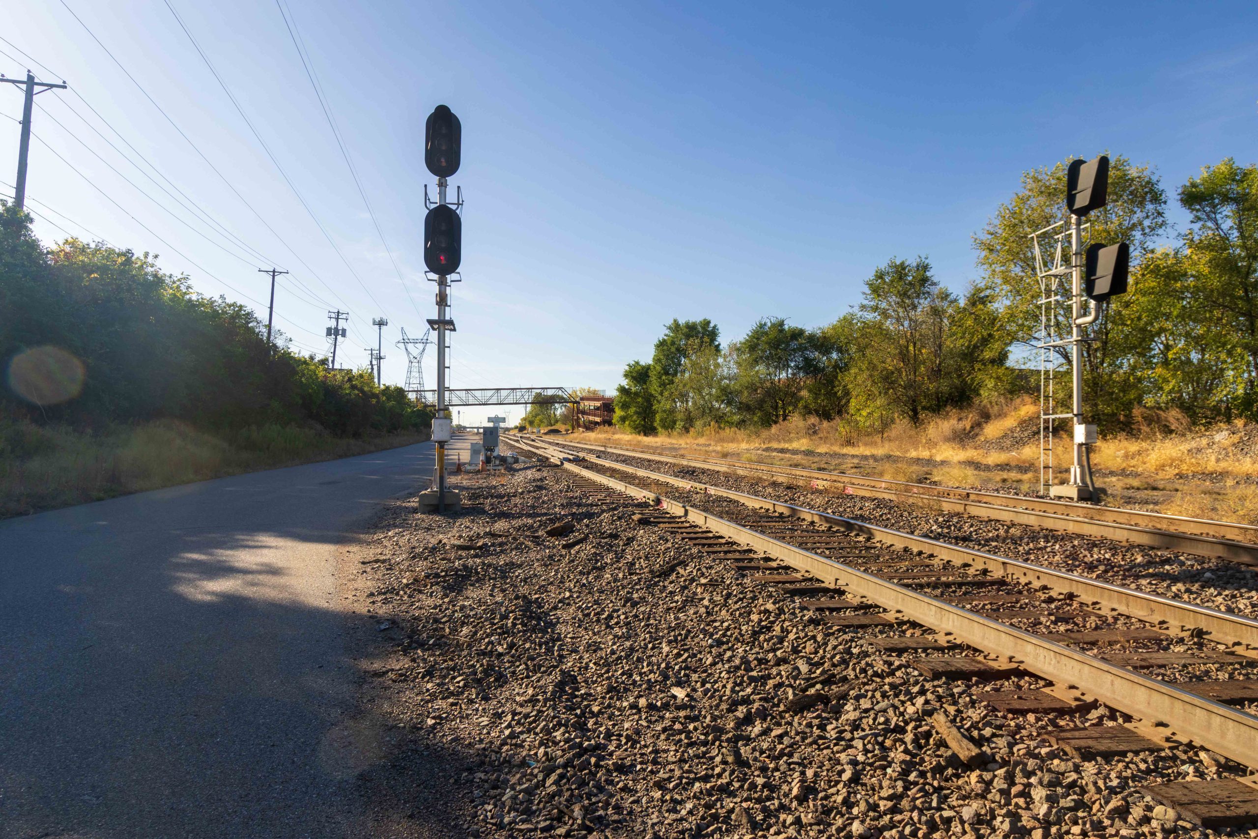 Paved road on the left; railroad tracks on the right; railroad signal in the middle.