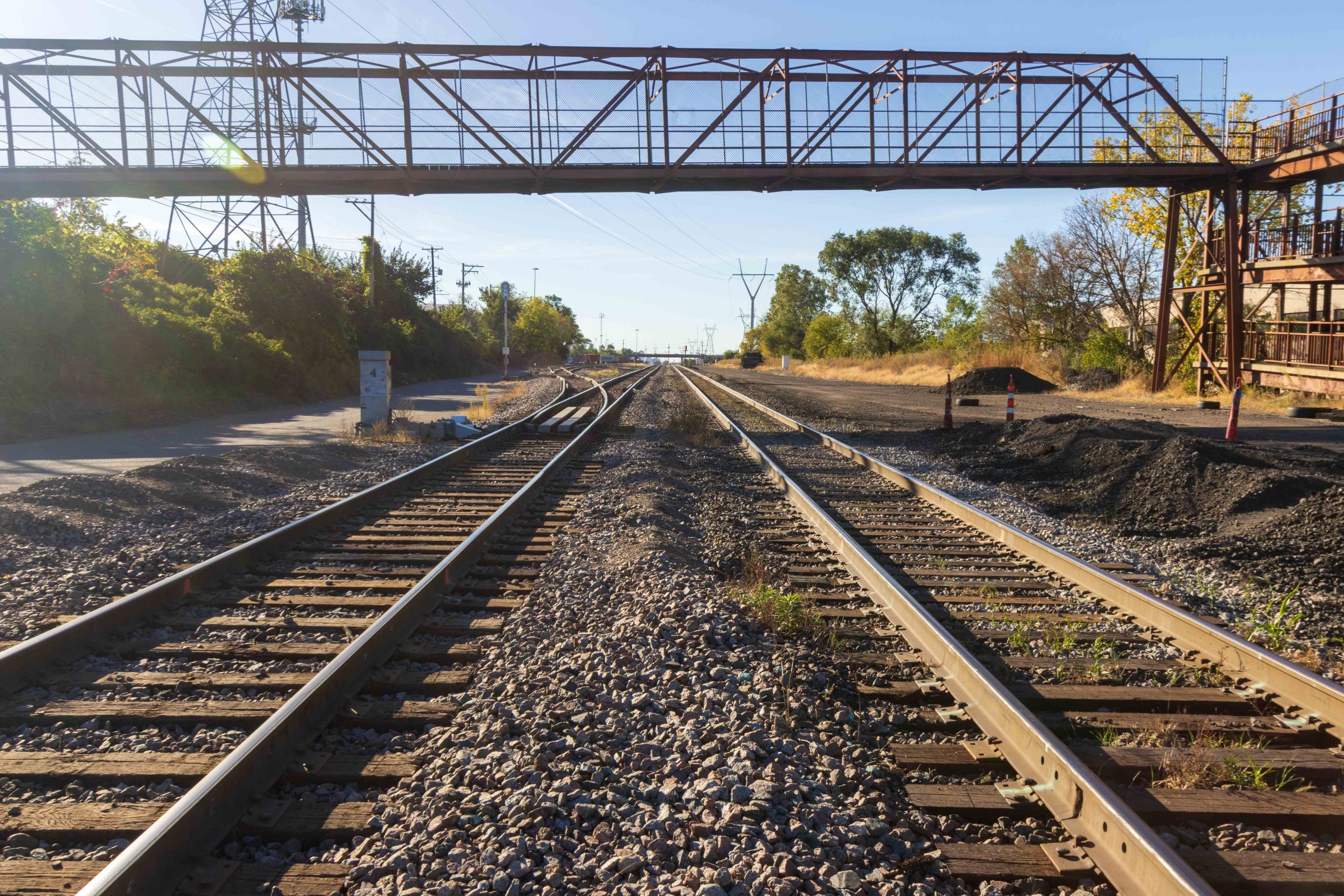 Railroad tracks heading off into the distance. Above, pedestrian/bike bridge over the tracks