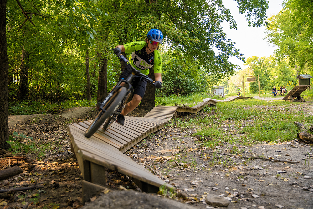A young bicyclist wearing a helmet navigates a twisting wooden boardwalk at the Kiwanis Recreation Area in Mankato