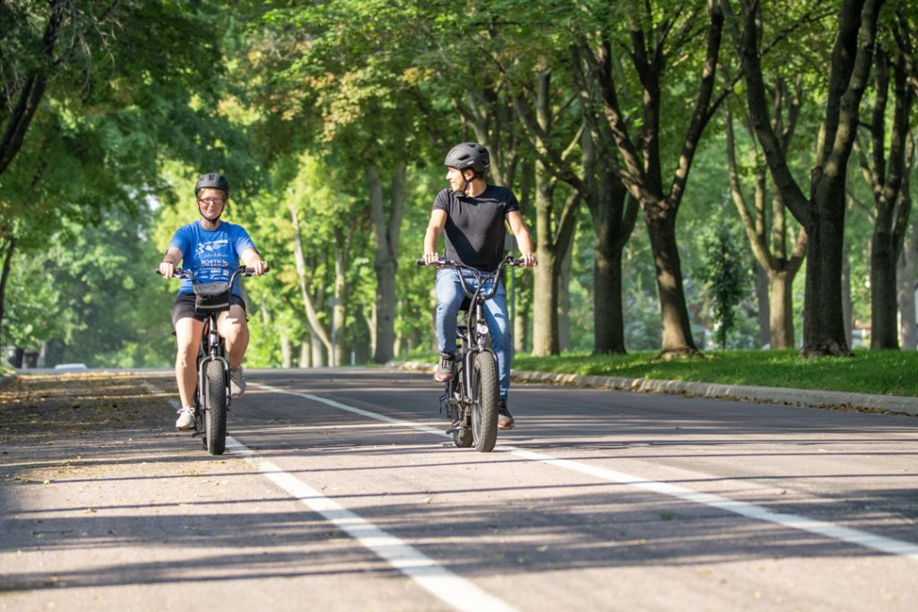 A woman and man ride bikes on painted lanes in a leafy neighborhood.