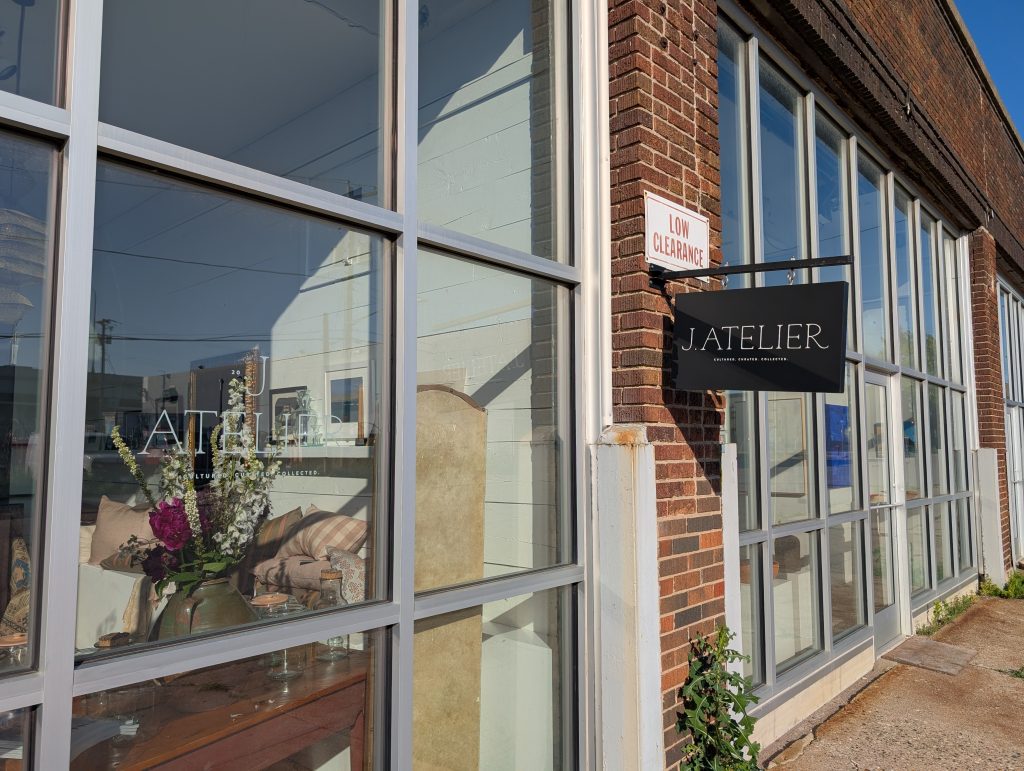 Brick-faced buidling with large metal and glass storefronts, one of which is signed J. ATELIER