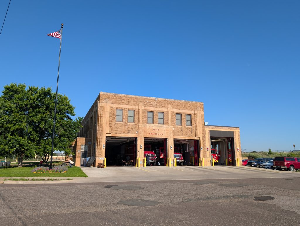 Three-bay two-story firehouse in a simple art deco style, captioned "M.F.D. STATION No 4" and with apparently newer additions on the left and right, the larger of which is the one on the right, which is a fourth bay