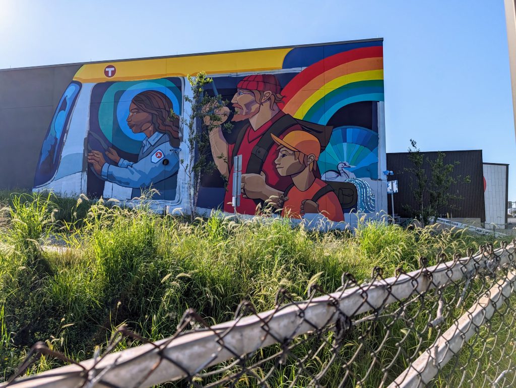 Building with mural showing front of MetroTransit bus with colorful, somewhat fantastic images visible through the windows, including a rainbow emanating from a backpack and extending out through the window