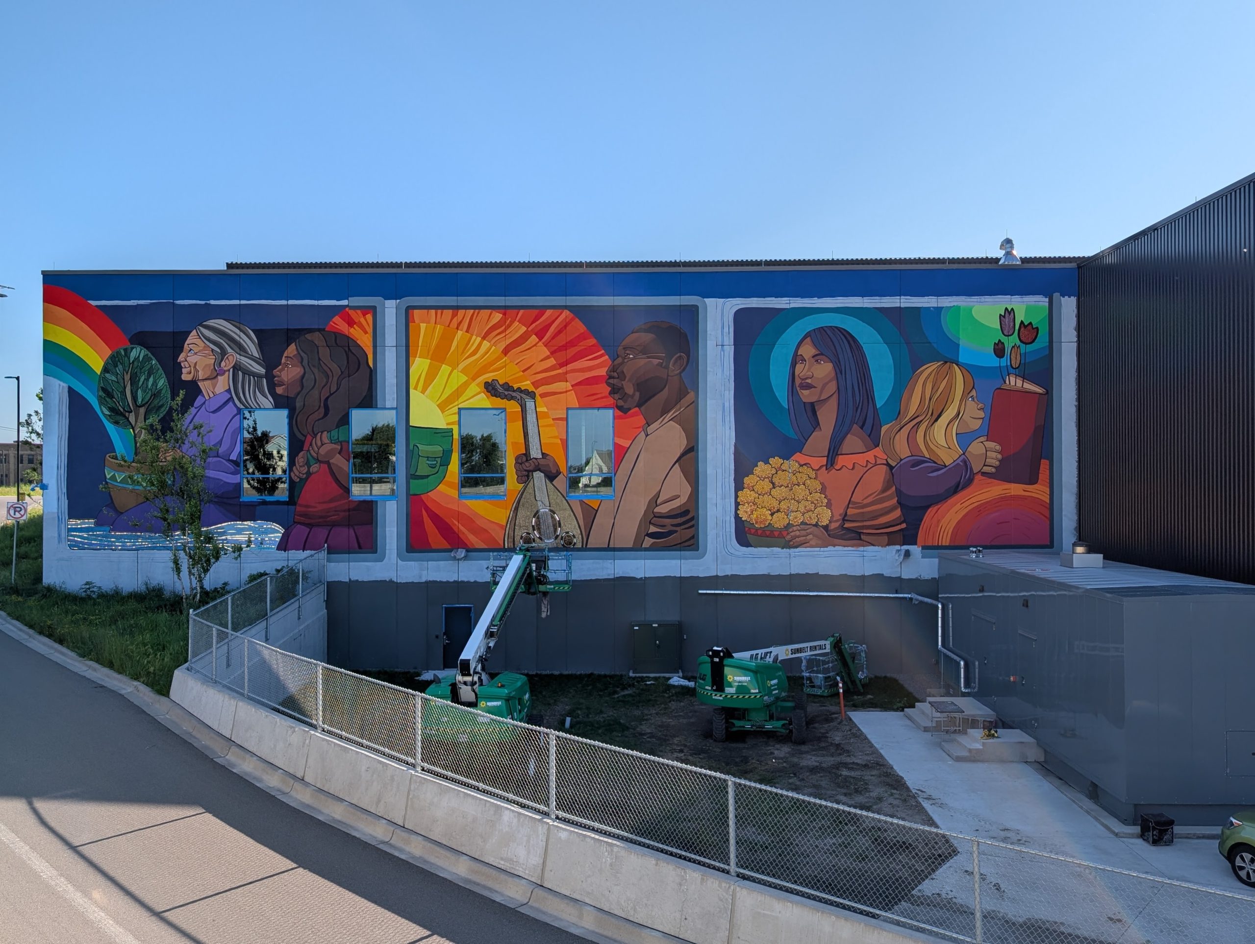 Building with mural of rear three windows of bus with more colorful, somewhat fantastic images, including the other end of the rainbow