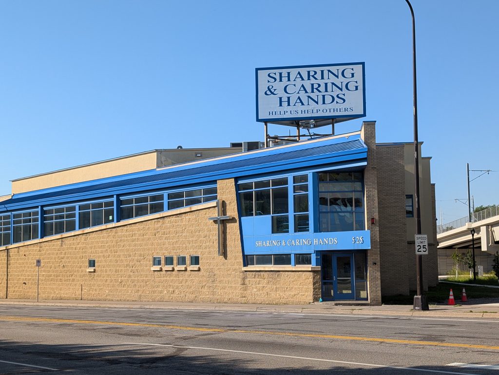 Building with a cross and signs indicating "SHARING & CARING HANDS" and "HELP US HELP OTHERS"