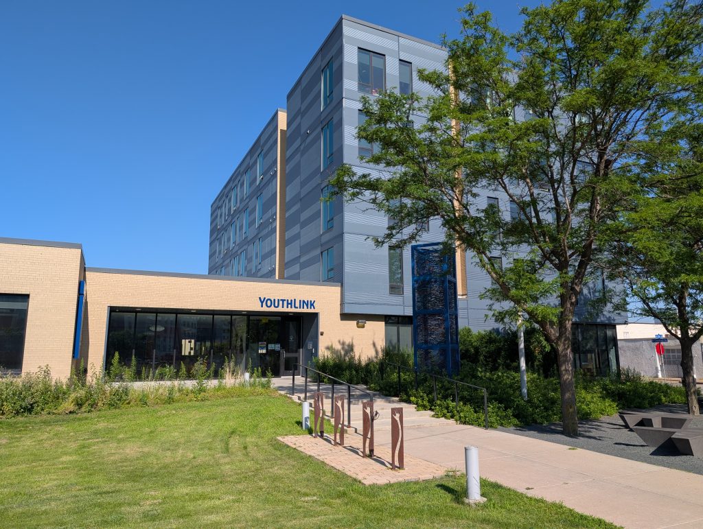 Conjoined one-story and five-story buildings; the one-story building is labeled YOUTHLINK; a sculptural bicycle rack is in the foreground