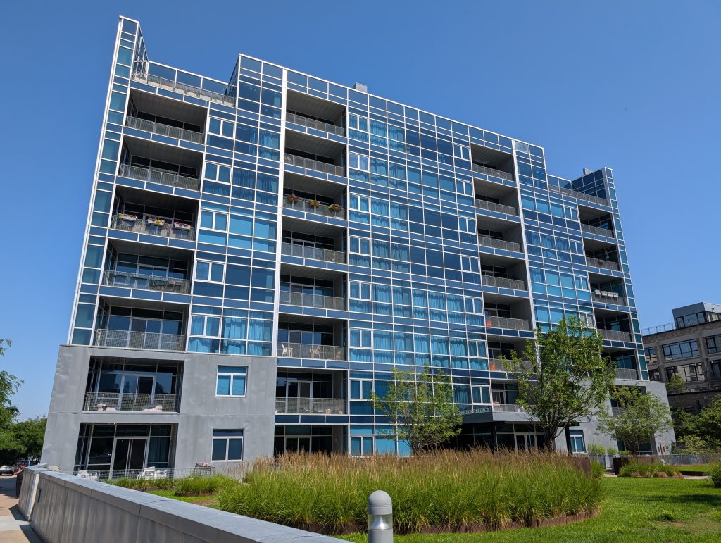 Modern condo building with balconies and a facade almost entirely of metal-framed blue-tinted windows