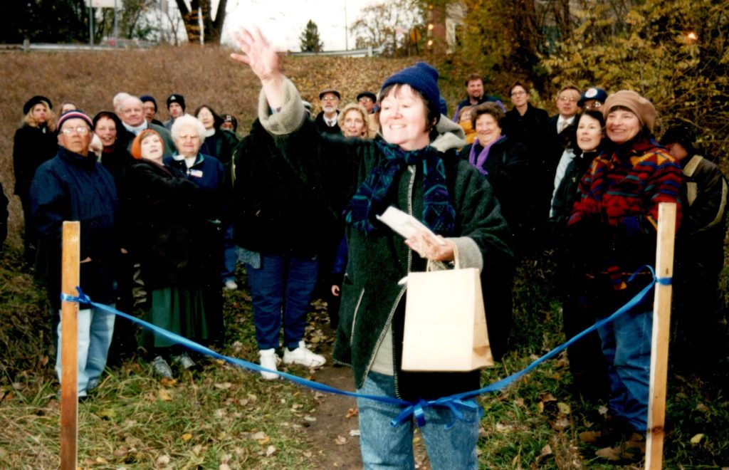 A group watches as a woman throws seeds as part of the blessing of the Trout Brook sanctuary.